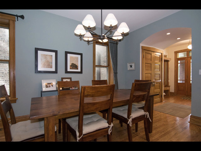 Dining room with blue walls, wooden table, chairs, chandelier, and framed artwork