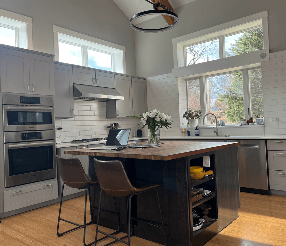 Modern kitchen with gray cabinetry, stainless steel appliances, island with wood countertop, and large windows