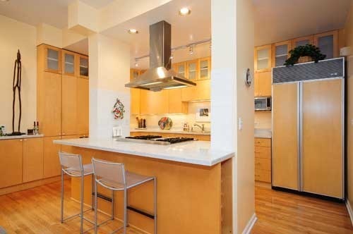 Modern kitchen with golden oak cabinetry, stainless steel appliances, and island seating