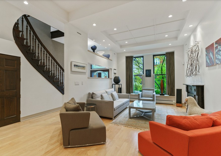 Modern living room with spiral staircase, neutral and orange seating, wood flooring, and large windows