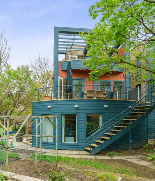Modern multi-level residential building with blue siding, orange brick upper section, and metal staircase