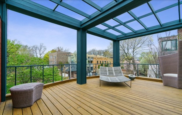 Modern rooftop deck with glass roof, wooden flooring, metal railing, and lounge furniture overlooking city
