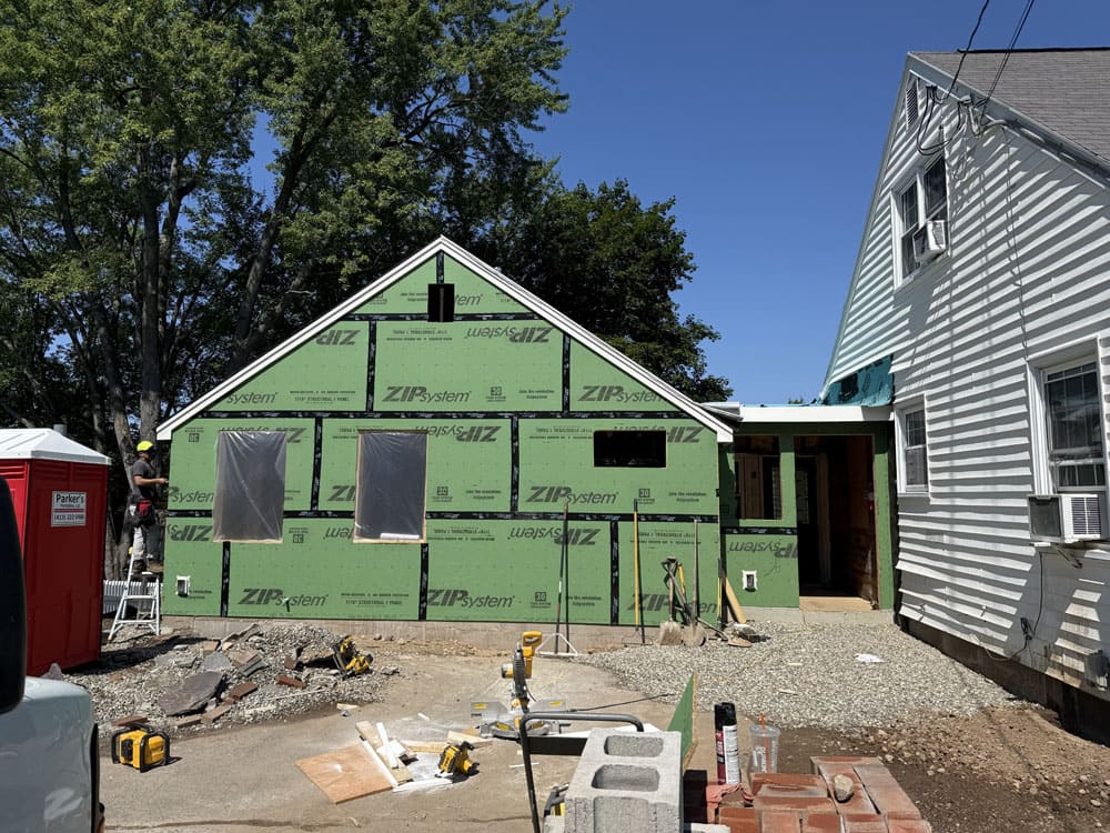 Home under construction with green ZIP system sheathing and adjacent finished houses