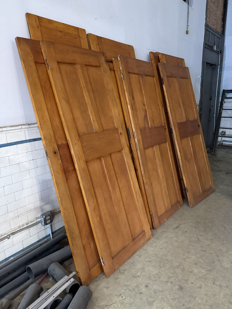 Vintage wooden cabinet doors leaning against white tile wall in warehouse setting