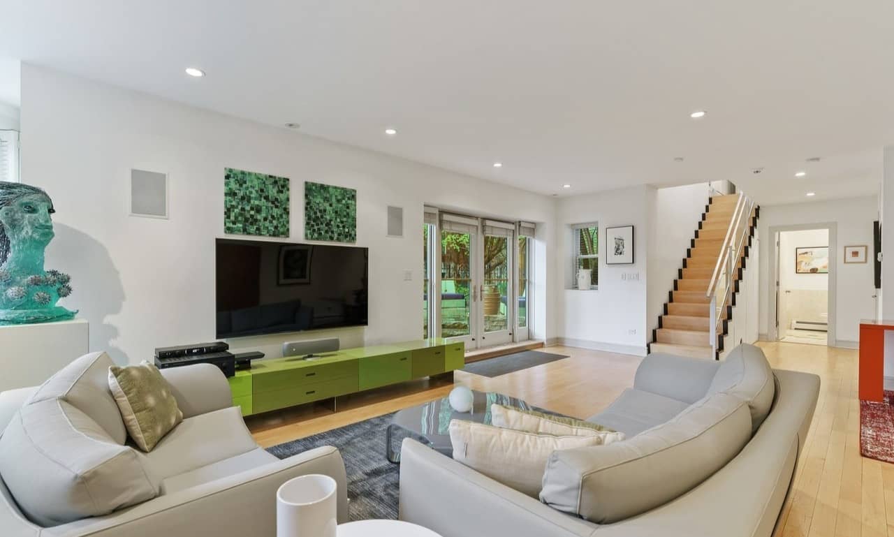 Modern living room with cream seating, green TV console, and staircase leading to upper floor